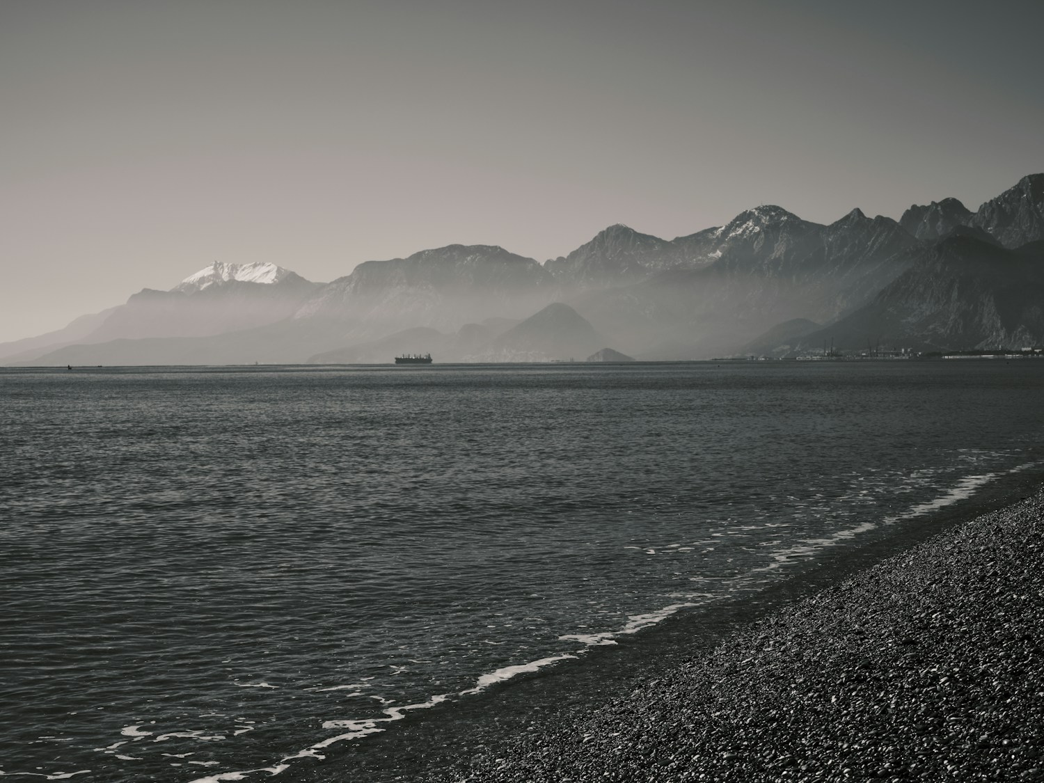 A monochrome coast beneath dramatic mountains